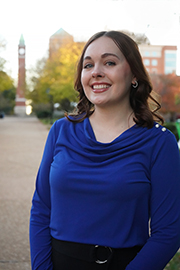 Headshot photo of Kit Bohn with a clocktower and trees in the background.