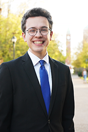 A headshot photo of Michael Poirier with a clocktower and trees in the background.