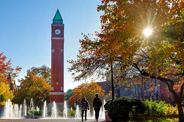 A group of students walk toward the SLU clock tower on a sunny fall day.