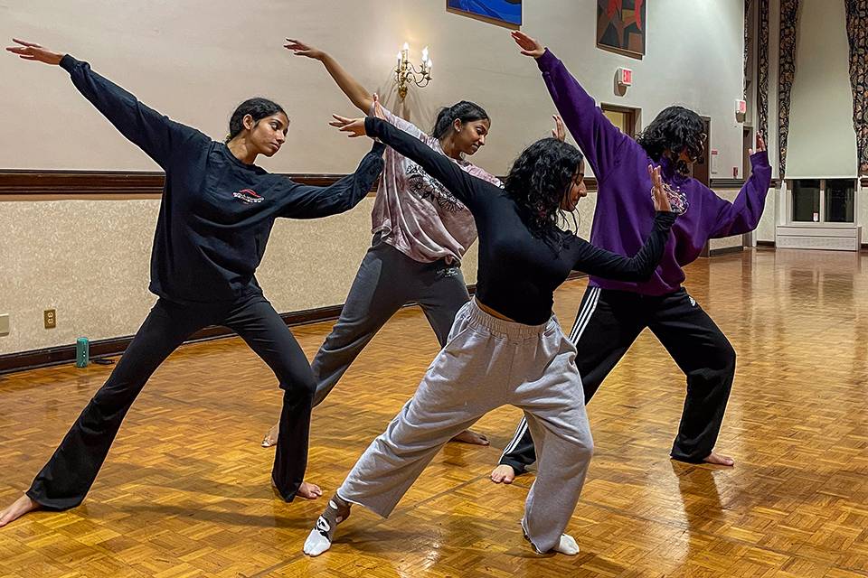 Four dancers lean on their left leg with their arms outstretched