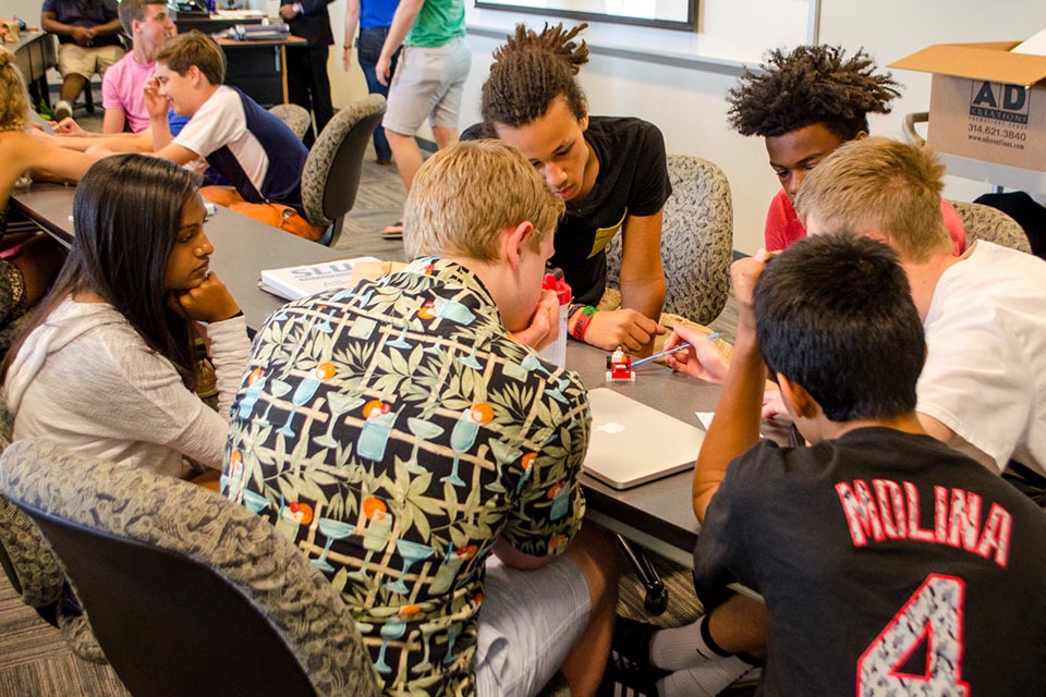 Student particpating in the Allsup Entrepreneurship Academy huddle around a table while they work together to solve an innovation challenge.