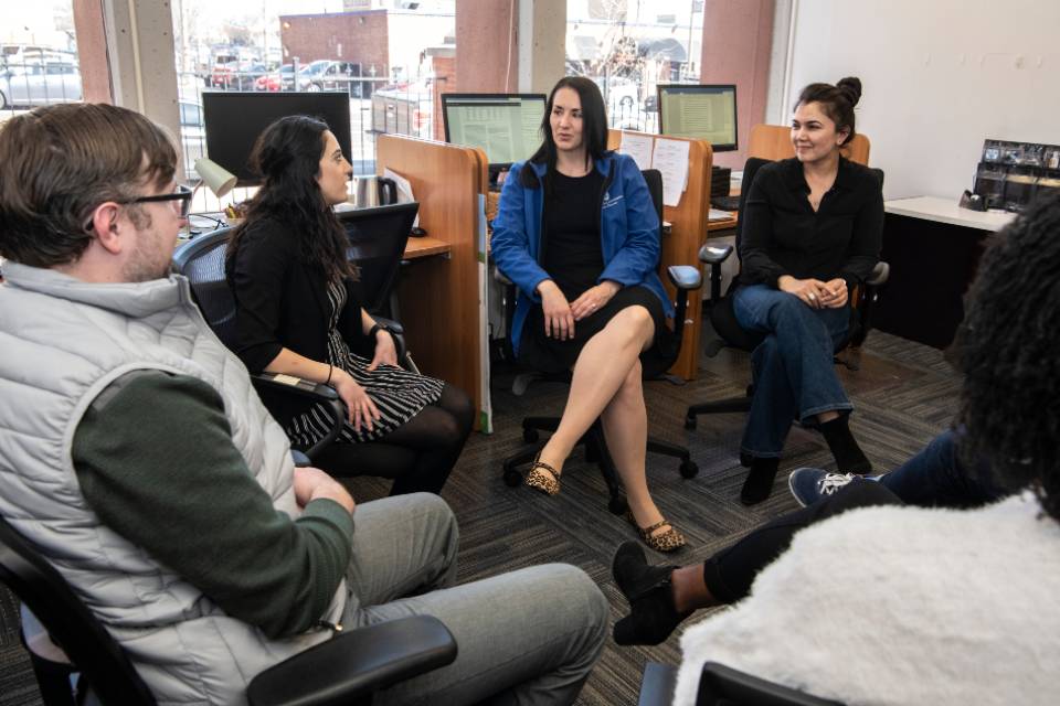 Four graduate students sit in a semi-circle having a discussion. 