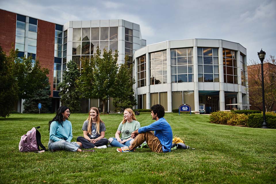 Students sit in a group on the grass field outside of the library.