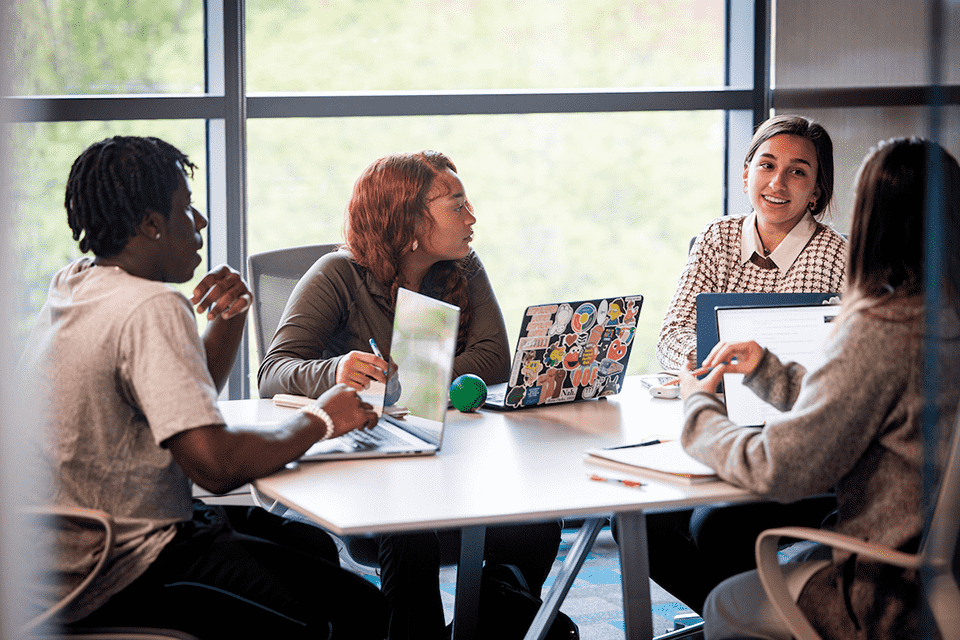 Four students with laptops sit around a conference table 