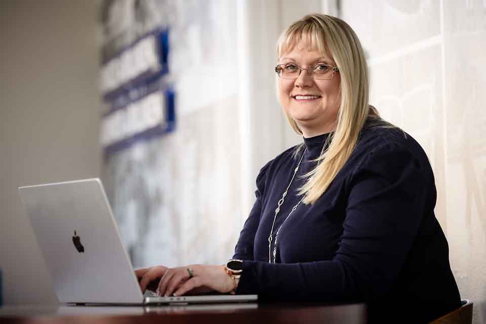 Ann Kelly sits at a table with a laptop