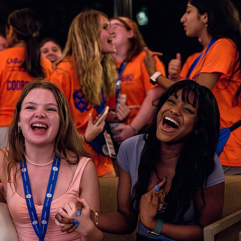 Two students are cheering while Oriflamme members in orange mingle behind them.