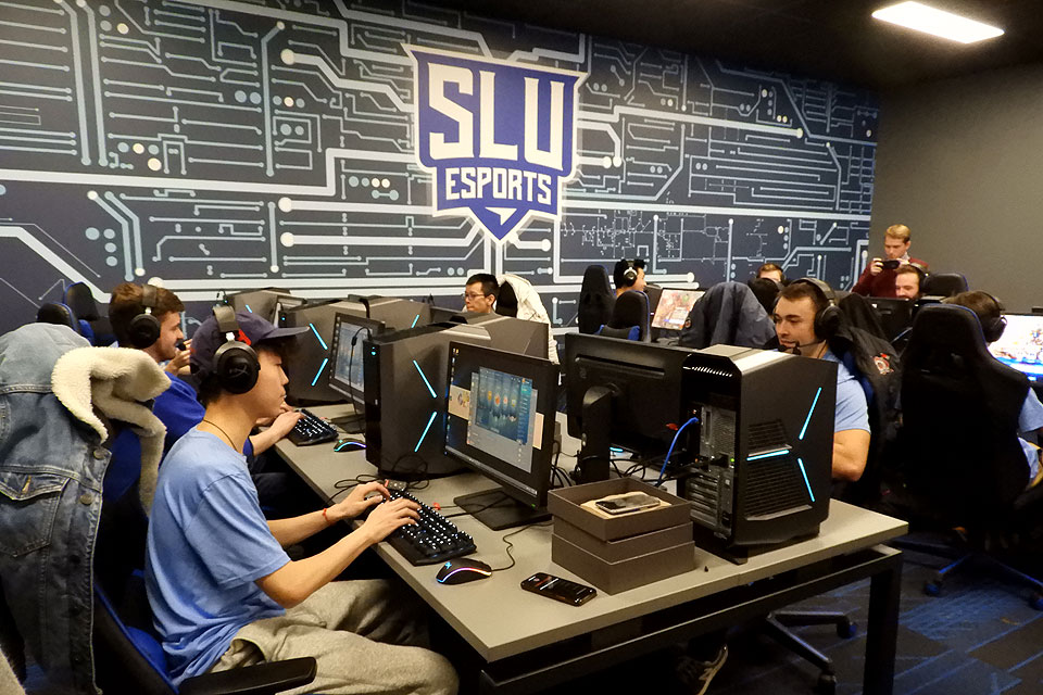 Esports players at two tables with headphones and CPUs with the eports logo in the background