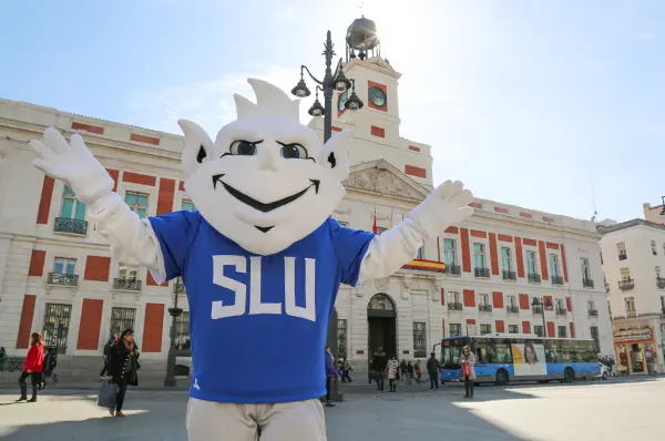 The Billiken stands in Madrid's central plaza, Puerta del Sol, surrounded by the bustling atmosphere of the city.