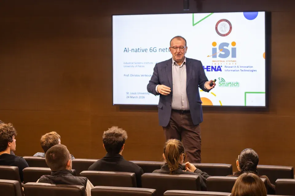 A man stands in front of a presentation screen discussing AI-native 6G networks while students sit in an auditorium watching and listening.