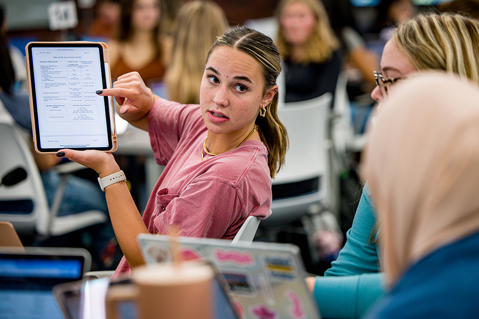 A student shows an iPad to two other students in class.