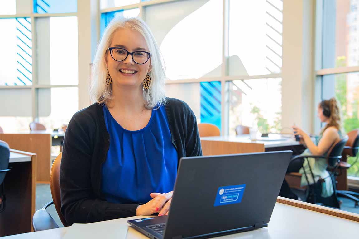 A woman sits in a library with a lap top in front her on a work table