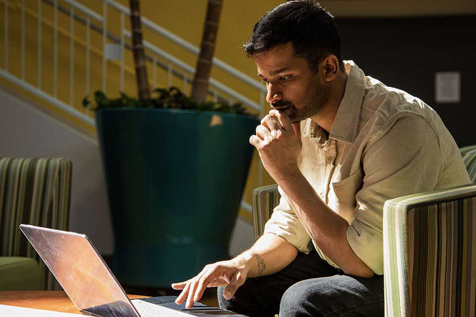 SLU STEM graduate, Akshay Mulera, studying on his laptop on campus. 