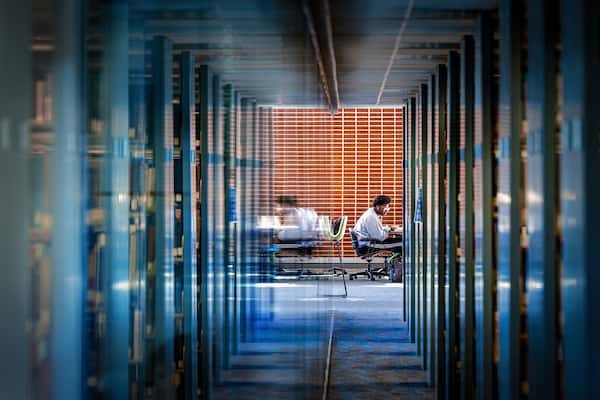 A student sits at a desk at the end of a hallway past dozens of shelves of books in Pius XII Memorial Library.