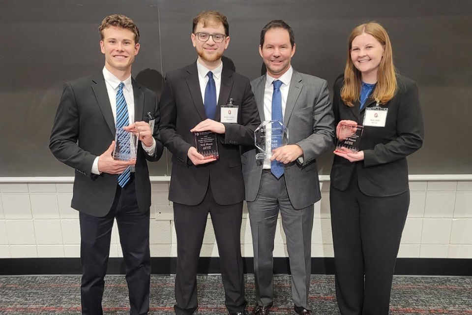 Four people in business attire pose while holding awards plaques.